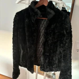 Svart pälsjacka - Säljer en supermjuk och fluffig svart pälsjacka. Perfekt för att hålla sig varm och stilren under kyliga dagar. Jackan har en quiltad insida och långa ärmar. Den är i mycket bra skick och redo för nya äventyr!