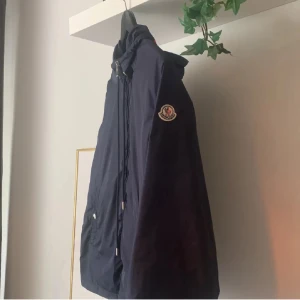  Moncler windbreaker - Säljer en snygg svart vindjacka från Moncler. Jackan har en huva och ett stilrent märke på ärmen. Storlek 1 vilket motsvarar S. Perfekt för blåsiga dagar och har en klassisk passform. Den är i mycket bra skick! Fler bilder kan ordnas vid seriöst intresse.