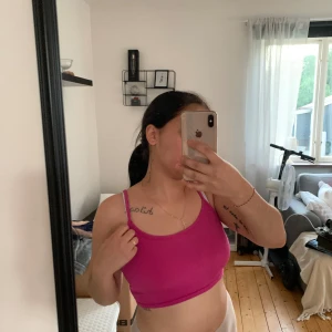 Rosa sport-bh - Säljer en rosa sport-bh som är perfekt för träning. Den är ärmlös och har en tight passform som ger bra stöd. Materialet är syntetiskt och den har en enkel design utan några extra detaljer.