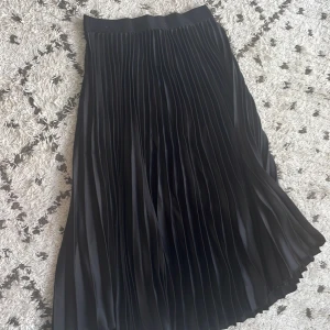 Svart plisserad kjol från H&M - Säljer en elegant svart plisserad kjol från H&M. Kjolen är i storlek M och har en fin glansig finish som ger en lyxig känsla. Perfekt för både vardag och fest! 🖤