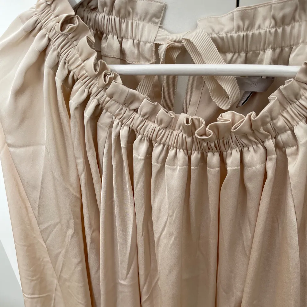 Beige blus från H&M med fina detaljer. Rosett i nacken som man kan knyta själv. Använd fåtal gånger. Storlek L. Puserot.