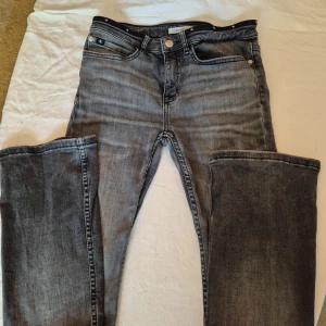 Grå jeans från Calvin Klein - Säljer ett par snygga grå jeans från Calvin Klein. De är i storlek 16 och har en klassisk femficksdesign med dragkedja och knapp framtill. Jeansen är i bra skick och har en cool tvättad look. Perfekta för både vardag och fest!