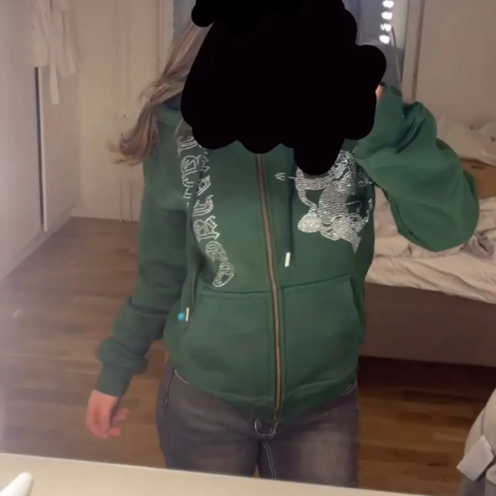 Säljer en grön hoodie med dragkedja med en textdesign på framsidan med rhinestones. Den har en luva och två fickor fram. Perfekt för en avslappnad och bekväm stil. Passar bra till jeans eller andra casual outfits. storlek : S. nypris ligger på 700kr men säljer för 400-500kr💚märke - laviago. Tröjor & Koftor.