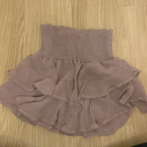 Ljuslila volangkjol - Säljer en superfin ljuslila volangkjol. Den är kort och har en elastisk midja som gör den bekväm att bära. Kjolen har flera lager av volanger som ger den en söt och lekfull look. Perfekt för sommarens fester eller bara en vanlig dag när du vill känna dig extra fin! 💜