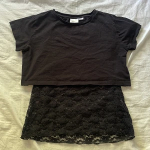 Svart croppad topp med spetsdetaljer - Säljer en svart croppad topp i storlek 146/164. Toppen består av två delar: en kortärmad överdel i bomull och en ärmlös underdel i spets. Perfekt för både vardag och fest! 🖤