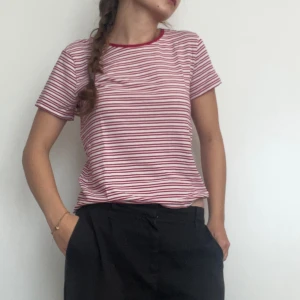 Röd- och vitrandig t-shirt från BikBok - Säljer en superfin röd- och vitrandig t-shirt från BikBok i storlek M. Den är gjord av mjuk bomull och har en normal passform. Perfekt för sommaren eller våren! T-shirten har korta ärmar och en rund halsringning med röd kant. Den är i nyskick och har knappt använts. Passar både till vardags och fest!