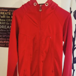 Röd jacka från WDRP - Säljer en snygg röd jacka från WDRP. Jackan har en dragkedja framtill och två fickor med dragkedjor. Den har en cool design med stora metallöljetter vid halsen. Perfekt för vår och höst!