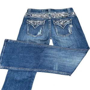 Vintage Miss Me bootcut jeans  - Säljer ett par blå vintage utsvängda lågmidjade jeans från Miss Me i storlek M eller W30, som har jättesnygga detaljer överallt, och har jättesnygga knappar som påminner mig lite om chrome hearts. Midja 38cm, innerbenslängd 83,5cm, längd 103,5cm