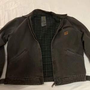 Carhartt Vintage Jacka - Säljer en svart jacka från Carhartt i storlek S/M. Jackan är tillverkad av bomull och polyester, med ett rutigt foder på insidan. Den har en dragkedja framtill och två fickor med dragkedja på sidorna. Priset kan diskuteras. Vid snabb affär 1500kr