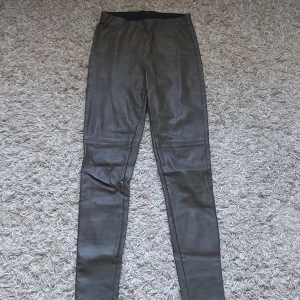 Svarta skinnleggings från HM - Säljer ett par mörkgröna skinnleggings från HM i storlek 38.. De är högmidjade och har en tight passform. Perfekta för en cool och edgy look! 🖤
