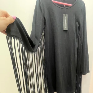 Svartklänning - Klänning med fransar, aldrig använd. Köpt för 299kr. Storlek XL men liten i storlek. 