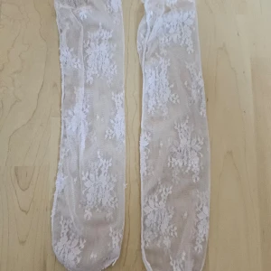 Vita spetsstrumpor - Säljer ett par vita spetsstrumpor i nyskick. De är supervackra med ett blommigt mönster och passar perfekt till både vardag och fest. Strumporna är genomskinliga och ger en elegant touch till vilken outfit som helst.