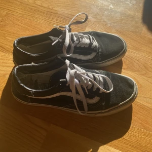 Svarta sneakers från Vans - Säljer ett par svarta Vans sneakers i välanvänt skick. De har den klassiska vita sidostripen och vita snören. Skorna har en vit sula som är lite smutsig, men de är fortfarande superbekväma och perfekta för vardagsbruk.