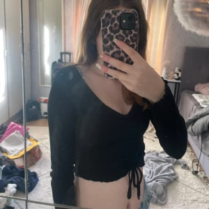 Svart croppad tröja - Säljer en svart croppad tröja med långa ärmar. Den har en snygg knytning framtill som ger en extra detalj. Perfekt för både vardag och fest! 🖤