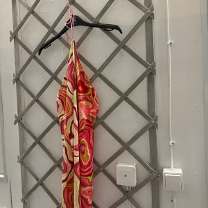 Klänning kolly - En kort, figursydd klänning med ett abstrakt mönster i röda, gula, gröna och vita toner. Klänningen har en halterneck. Den är från kolly och använd fåtal gånger men är i riktigt bra sick!