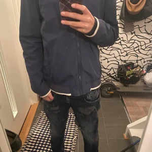 Blå bomberjacka från Polo Ralph Lauren - Säljer en snygg blå bomberjacka från Polo Ralph Lauren. Jackan har en dragkedja framtill och är långärmad. Den har en klassisk design med en liten röd logga på bröstet. Perfekt för vår och höst!