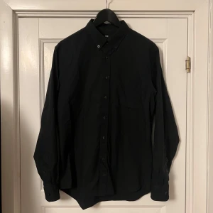 Svart skjorta från Uniqlo - Säljer en stilren mörkblå skjorta från Uniqlo i storlek S. Skjortan är långärmad och har en klassisk krage med knappar hela vägen ner. Perfekt för både vardag och fest!