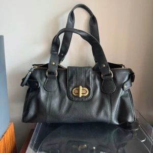 Svart väska  - En svart jättefin väska! Mellanstor ( 34x12 cm ungefär)  Har en liten skada som syns på sista bilden men funkar att använda ändå.