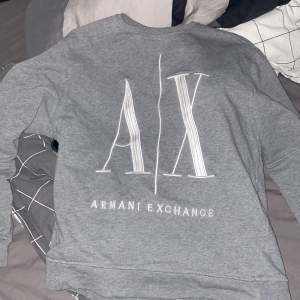 Säljer en snygg grå tröja från Armani Exchange. Den har en stor A|X-logga på framsidan och är i storlek M. Perfekt för en casual look och passar till alla tillfällen. Tröjan är i bra skick och superbekväm att ha på sig.