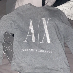 Grå tröja från Armani Exchange - Säljer en snygg grå tröja från Armani Exchange. Den har en stor A|X-logga på framsidan och är i storlek M. Perfekt för en casual look och passar till alla tillfällen. Tröjan är i bra skick och superbekväm att ha på sig.