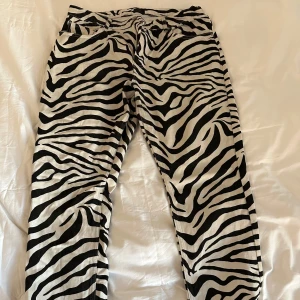 Zebramönstrade jeans - Ett par supersnygga jeans med zebramönster från Nelly. Storlek 44, ingen stretch! Har en snygg slits nere vid benens slut🩷 Gott skick men finns någon liten fläck vid benet (som går bort i tvätten). Så inne med djurmönster nu, slå till!😻
