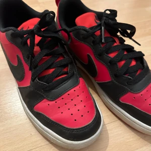 Nike sneakers i rött och svart - Säljer ett par snygga Nike sneakers i rött och svart. De har en klassisk design med snörning och en bekväm passform. Perfekta för vardagsbruk eller träning. Skorna är i bra skick med lite slitage på sulorna.