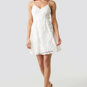 NA-KD Vit spetsklänning med smala axelband - Säljer en vacker vit klänning med smala axelband och spetsdetaljer. Klänningen har en v-ringad design och är perfekt för sommarens festligheter.  Fint skick. Storlek 36. Se gärna mina andra annonser för fler sommarkläder.