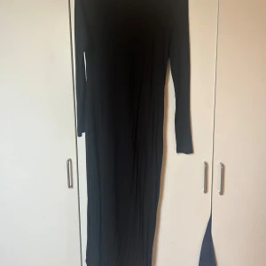 Svart långklänning - Elegant svart långklänning med långärmad design. Perfekt för en stilren look. Klänningen har en enkel och tidlös stil som passar till många tillfällen.