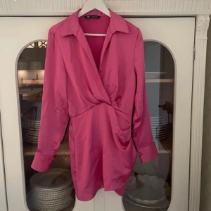 Rosa omlottklänning från Zara - Snygg rosa omlottklänning från Zara med långa ärmar och en elegant krage. Perfekt för en chic look med sin omlottdesign. Passar utmärkt för både vardag och festliga tillfällen. Använd 1 gång och är i nyskick 