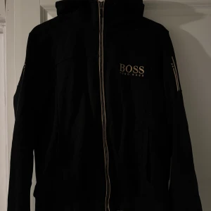 Svart hoodie från Hugo Boss - Säljer en stilren svart hoodie från Hugo Boss med dragkedja och luva, tröjan är i bra skick endast använd fåtal gånger, storlek m har du fler frågor tveka inte att höra av dig🤝🏽