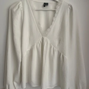 Vit blus från Vero Moda - Säljer en söt vit blus från Vero Moda med spetsdetaljer vid v-ringningen. Blusen har långa ärmar och en lös passform som ger en avslappnad look. Perfekt för en stilren och bekväm outfit. XS men passar även S. Använd ett par gånger men är i fint skick! ❣️