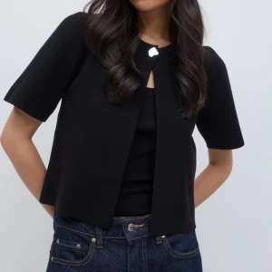 Svart kortärmad ”kofta” från Gina tricot - Snygg svart kortärmad ”kofta” från Gina tricot med en enkel knäppning framtill. Den är tillverkad i viskos, oanvänd med prislapp kvar. Köpt för 399 