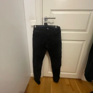 Svarta jeansbyxor - Snygga svarta jeansbyxor med en tight passform. De har en klassisk design med knappar och dragkedja framtill. Perfekta för en stilren look.