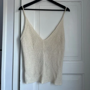 Beige stickad linnetopp - Säljer en stilren beige stickad linnetopp med smala axelband och v-ringning. Perfekt för varma dagar och kan enkelt matchas med olika outfits. Toppen har en mjuk och bekväm passform.