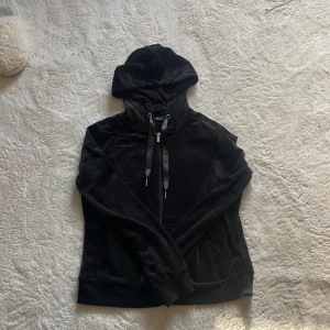 Svart hoodie med dragkedja - Säljer en stilren svart hoodie med dragkedja och justerbar huva. Perfekt för en avslappnad look. Den har långa ärmar och en praktisk ficka framtill. Passar bra till både jeans och träningsbyxor.