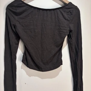 Svart långärmad topp - Snygg svart långärmad topp med öppen rygg. Perfekt för en stilren look. Toppen är i ett mjukt och stretchigt material som ger en bekväm passform.
