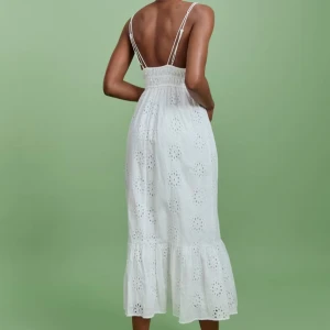 Vit sommarklänning med spetsdetaljer - Charmig vit klänning med smala axelband och v-ringning. Klänningen har ett vackert spetsmönster och volangdetalj vid fållen. Perfekt för varma sommardagar.
