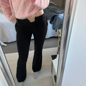 Lågmidjade kostymbyxor - Snygga svarta byxor med bootcut-stil. De har en lågmidjad passform och är perfekta för en stilren look. Byxorna har en klassisk design med knappar och dragkedja framtill. Den är från design by si! Säljs inte längre!💗 Jag är 170 cm lång!