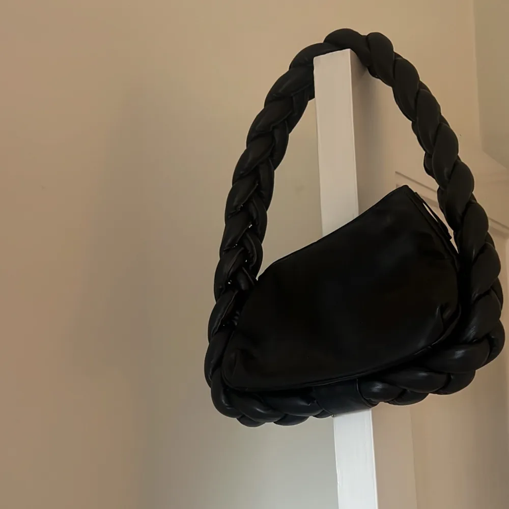 Snygg svart axelväska med ett unikt flätat handtag. Väskan har en dragkedja för säker förvaring och är tillverkad i skinn. Perfekt för att ge din outfit en stilren touch.. Laukut & Käsilaukut.