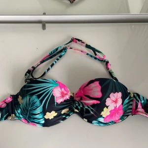 Blommig bikini med knytband har inte kommit till användning 💗 - Snygg bikini med tropiskt blommönster i rosa och grönt på en svart bakgrund. Den har avtagbara knytband. Perfekt för en dag på stranden eller vid poolen.