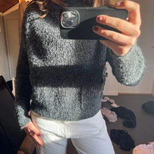 Grå stickad tröja - Säljer en mysig grå stickad tröja med hög krage. Tröjan har en avslappnad passform och långa ärmar, perfekt för kyligare dagar. Den är enkel att matcha med olika outfits och ger en stilren look.
