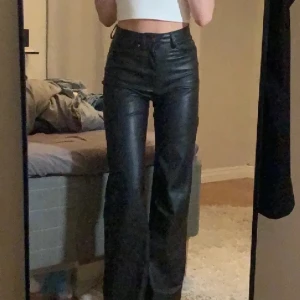 Svarta skinnbyxor - Snygga svarta skinnbyxor med hög midja och en rak passform. Byxorna har en klassisk design med fickor och knappar framtill. Perfekta för en stilren look.