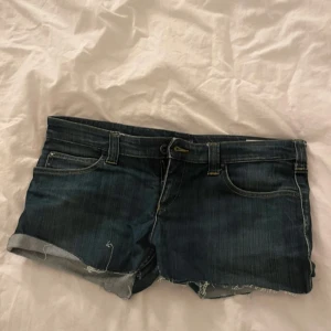 Jeansshorts från Armani Jeans - Snygga jeansshorts från Armani Jeans i en klassisk blå färg. De har en lågmidjad design med fransiga kanter och dragkedjor på bakfickorna för en cool look. Perfekta för sommardagar!