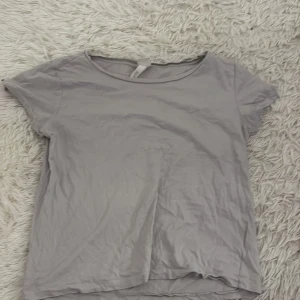 Grå/beige t-shirt - En enkel och stilren grå t-shirt med rund halsringning och korta ärmar. Perfekt för en avslappnad look.