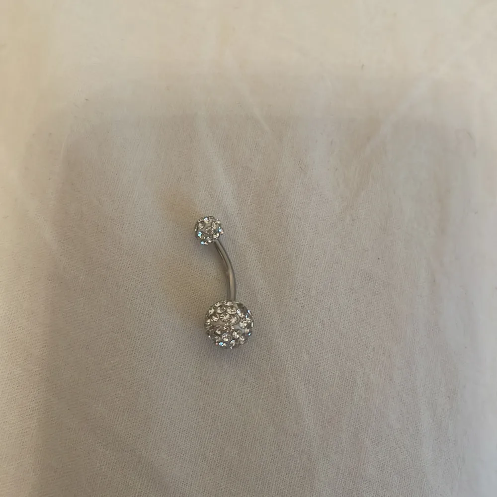 Snygg navelpiercing med två glittriga kulor i silverfärg. Perfekt för att ge lite extra bling till din stil. Passar bra till både vardag och festliga tillfällen.. Asusteet.