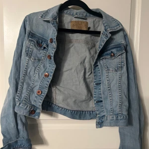 Ljusblå jeansjacka - Säljer en klassisk ljusblå jeansjacka med knappar framtill och två bröstfickor. Jackan har en normal passform och är perfekt för vår och sommar. Den har långa ärmar och en stilren design som passar till det mesta. Perfekt för en avslappnad look! 💙