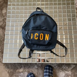Blå ryggsäck Dsquared2 - Snygg blå ryggsäck från Dsquared2 med texten 'ICON' i gult på framsidan. Ryggsäcken har en praktisk dragkedja och justerbara axelremmar. Perfekt till skolan eller bara ner till stranden