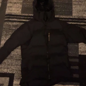 Svart dunjacka från Sail Racing - Säljer en svart dunjacka från Sail Racing, perfekt för kalla dagar. Jackan har en dragkedja framtill och en huva för extra skydd. Den är en del av Sail Antarctica Expedition-kollektionen, vilket gör den både stilren och funktionell.