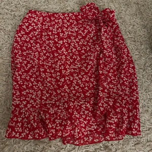 Röd blommig kjol med knytband - Charmig röd kjol med vita blommor och knytband i midjan. Kjolen har en volangdetalj vid fållen som ger en lekfull touch. Perfekt för en somrig look! Fraktar endast varan och köparen betalar frakten! Priset som syns är vad som gäller🙏🫶