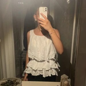 Vit ärmlös topp med volanger - Säljer en söt vit ärmlös topp med volanger. Perfekt för sommardagar och kan enkelt matchas med jeans eller kjol. Toppen har en luftig passform och är i storlek s men skulle även säga storlek m. Hör gärna av dig för fler bilder! 